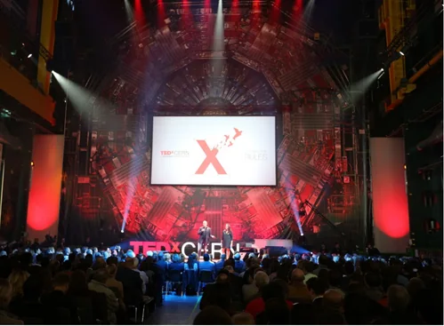 Conférence TEDx CERN, scène éclairée en rouge devant un public nombreux
